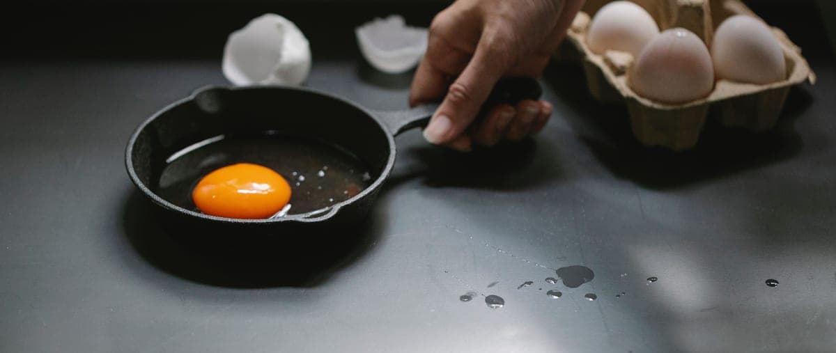 A cast iron skillet being cleaned under running water with a brush