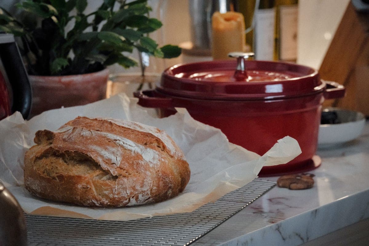 A crusty round loaf of bread lifted from a dutch oven